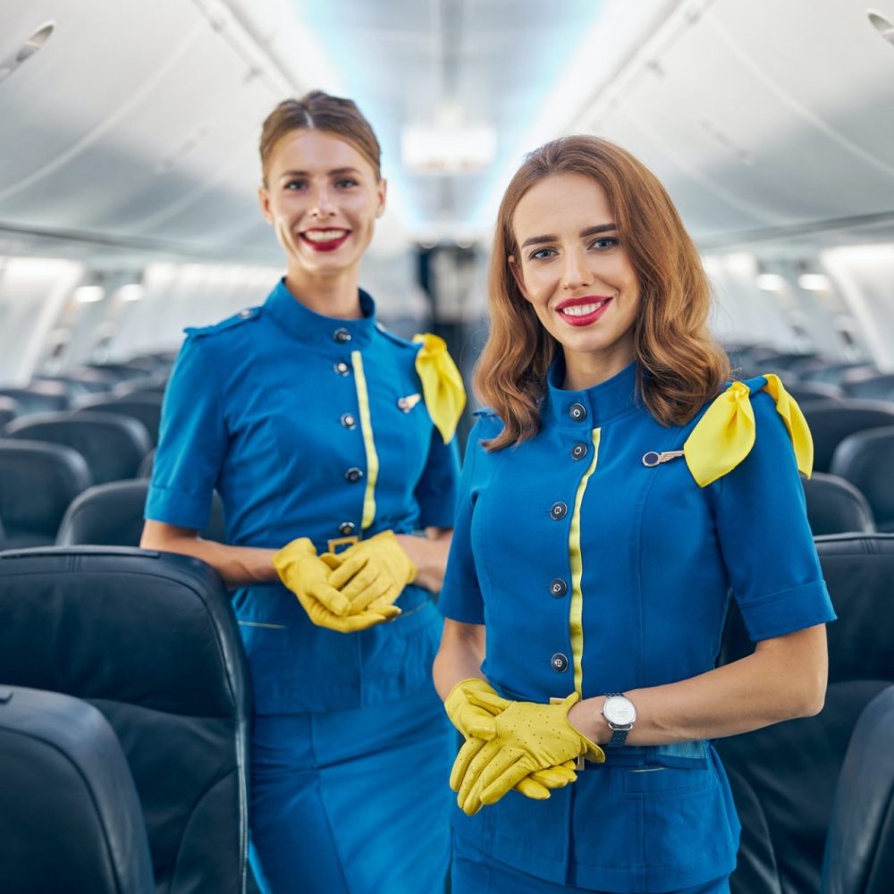 two-women-flight-attendants-smiling-at-the-photo-camera-in-salon-of-passenger-aircraft-e1630651564416.jpg